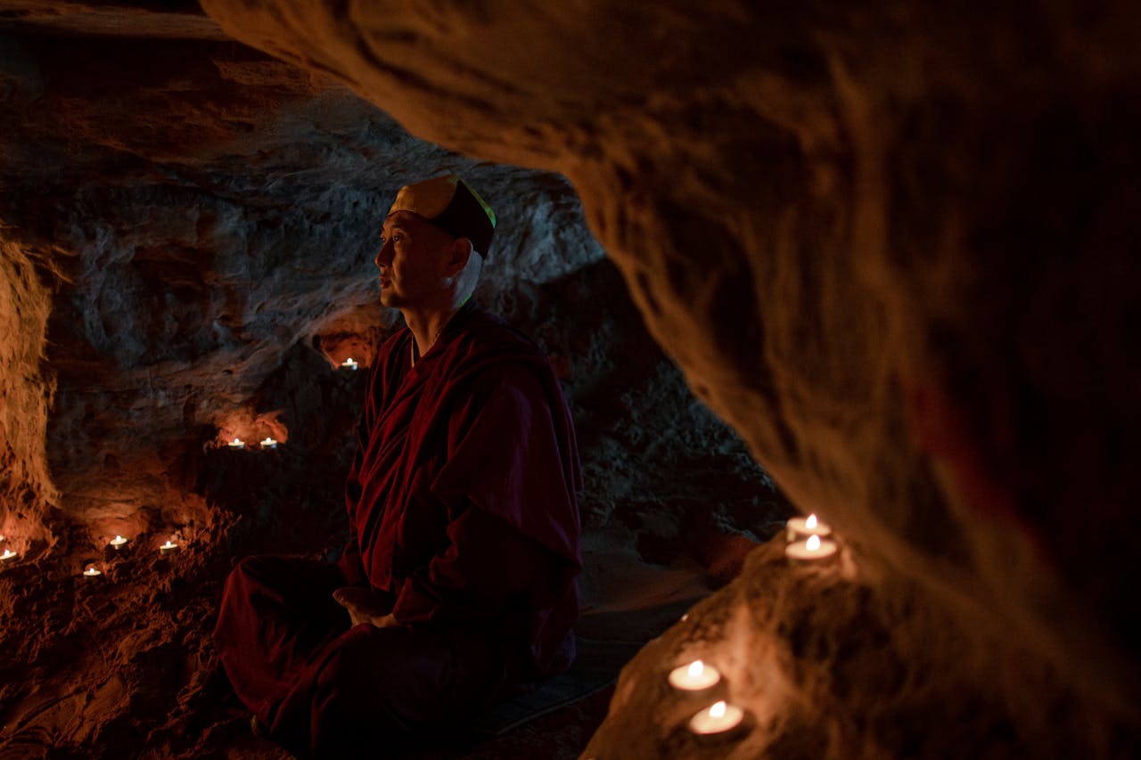 A serene monk meditates in a candle-lit cave, embracing tranquility.